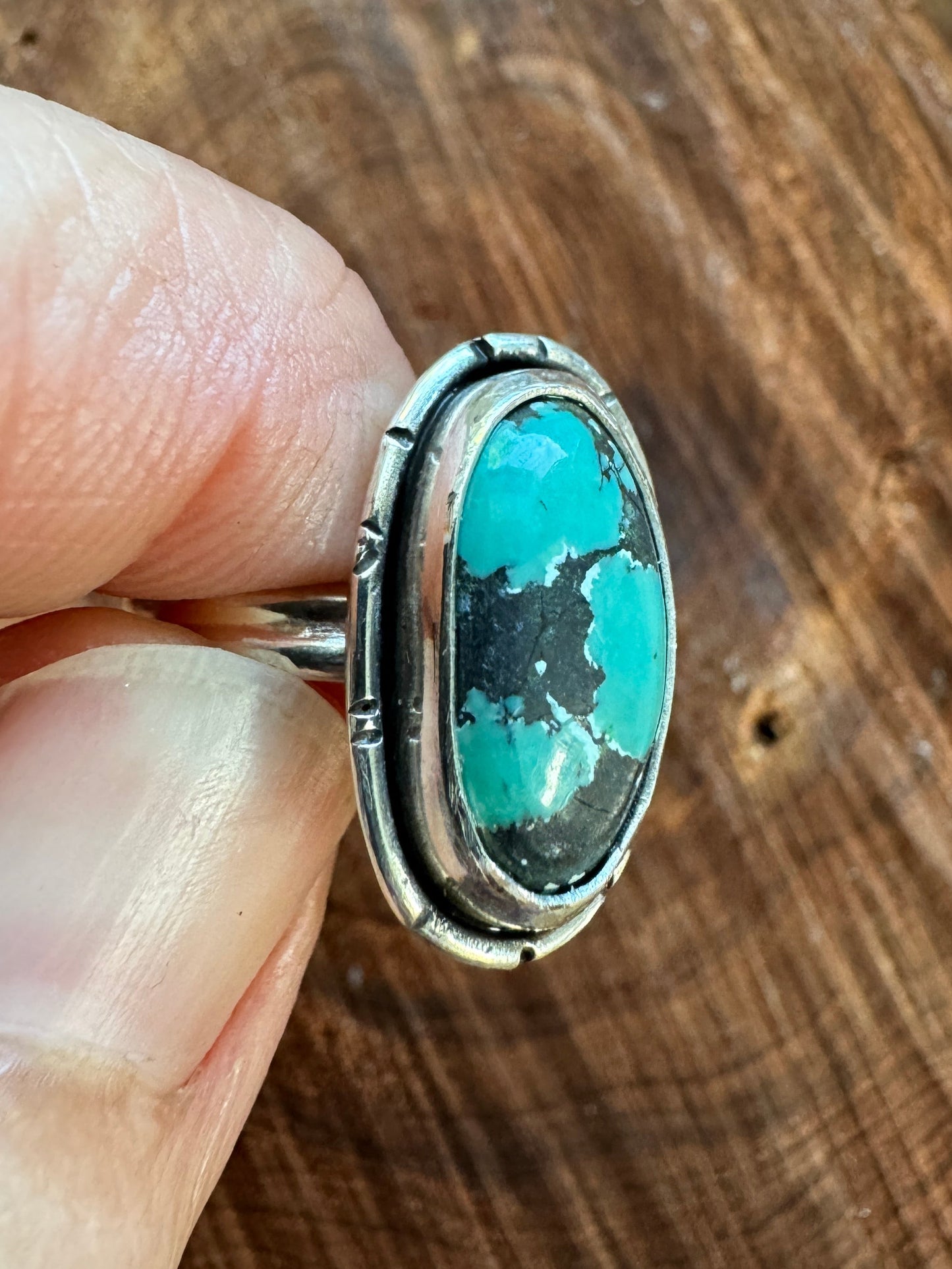 Turquoise ring held in a hand against a wooden background