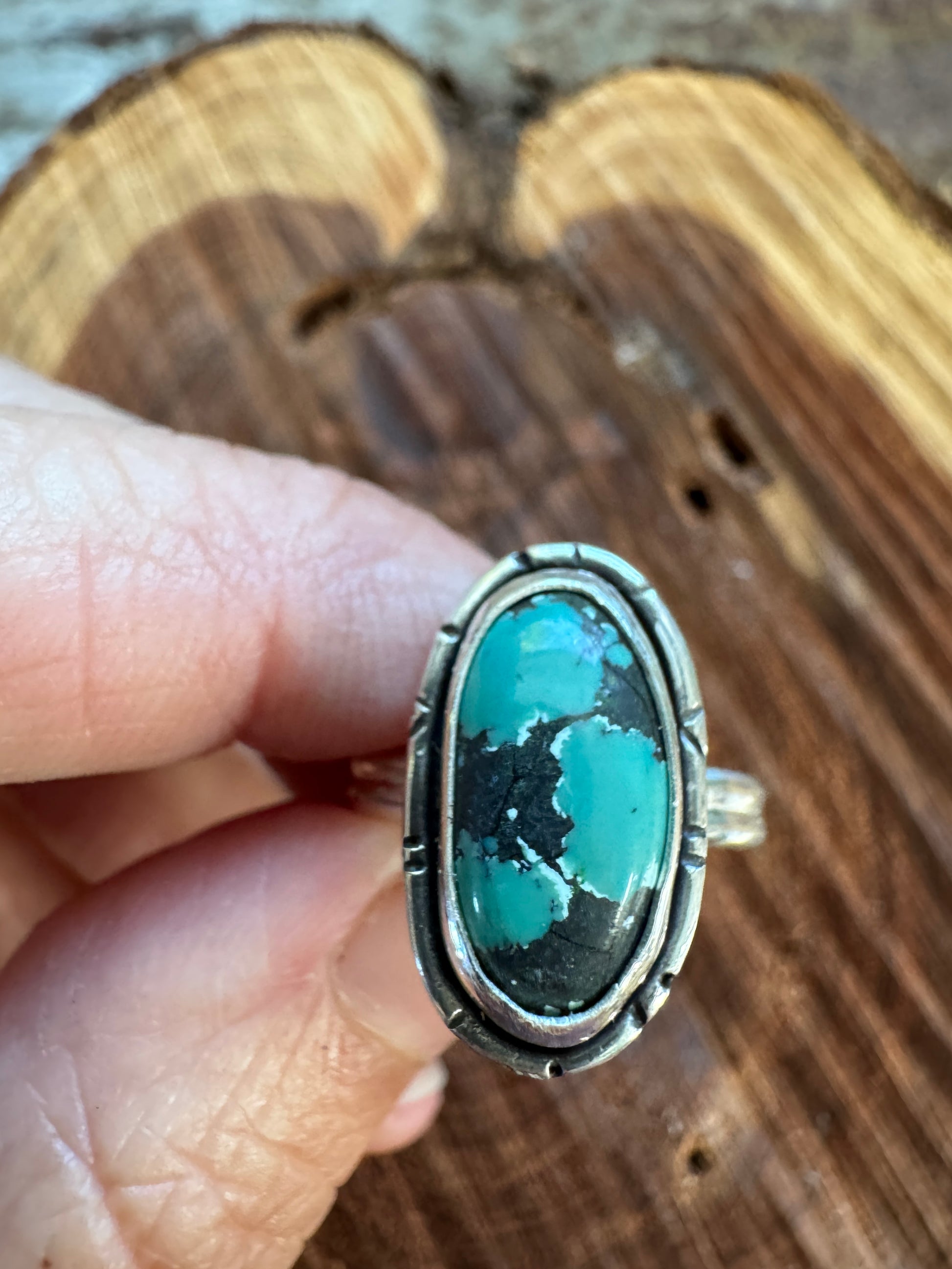 Turquoise ring with silver setting held by a hand on a wooden surface